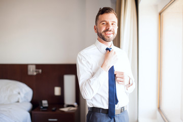 Wall Mural - Latin businessman fixing his tie in a hotel