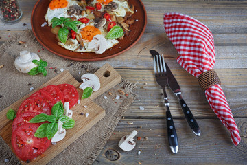 Fried eggs with mushrooms, tomatoes and basil on rustic wooden t