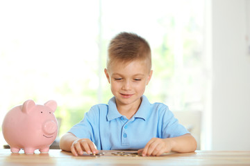 Poster - Savings concept. Little boy counting coins at table with piggy bank