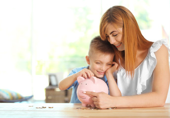 Poster - Savings concept. Mother and little boy putting coins into piggy bank