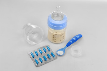 Fototapete - Baby milk bottle with spoon and pills on white background