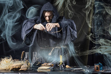 Halloween. The Medieval Alchemist Holds Magic Ritual At The Table In His Laboratory Smoke In The Background
