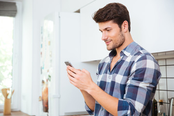 Handsome young man standing and using smartphone on the kitchen