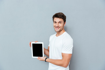 Poster - Smiling handsome young man standing and holding blank screen tablet