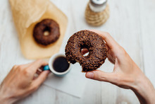 Man Hands Eating Chocolate Donut With Coffee On Wooden Table
