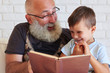 © ArtFamily - Portrait of grandfather and his small grandson reading a book to