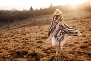 Canvas Print - happy boho woman, walking towards sun, wearing hat and poncho at