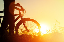 Silhouette Of Young Woman Riding Bike At Sunset