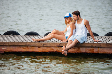 Wall Mural - Couple sitting barefoot and talking on pier