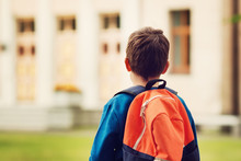 Boy With Rucksack Infront Of A School Building. Child With A Backpack