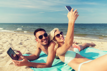 Wall Mural - happy couple with modern gadgets lying on beach