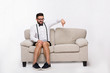 © Svyatoslav Lypynskyy - Picture of surprised handsome hipster man pointing down while sitting on sofa or couch isolated on white background in studio. Studio shot.