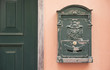 Green metal letterbox beside a green door over a pink wall - Classic vintage letterbox - Italian decor style