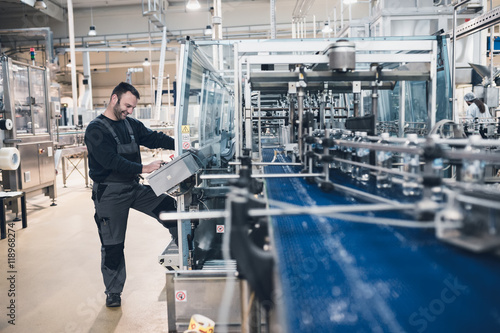 Fotografía Happy smiled worker doing his job on Robotic factory line for processing and quality control of pure spring water bottled into canisters