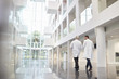 Leinwandbild Motiv Rear View Of Doctors Talking As They Walk Through Hospital