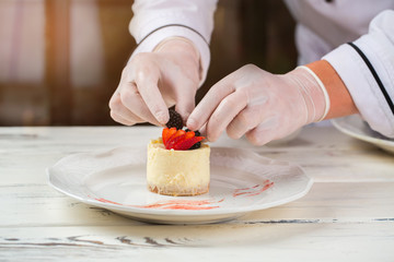 Hands in gloves hold berries. Slices of strawberry on dessert. Mousse cake made by chef. Sweet dish on white table.