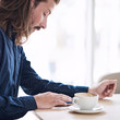© nakophotography - Square image of handsome caucasian man with long brown hair using tablet that is lying on the table in front of him next to his coffee.