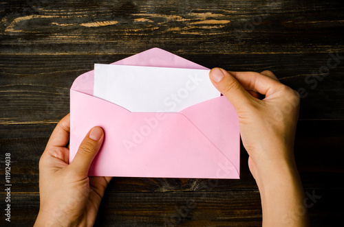 Fotografia, Obraz Pink envelope and blank white card are hold by hand on wooden background