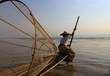 Burmese fisherman on bamboo boat catching fish in traditional way with handmade net. Inle lake, Myanmar (Burma)