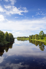 Wall Mural - Calm evening at the river. Forest and boats are reflecting from the still water. Blue sky with some clouds.