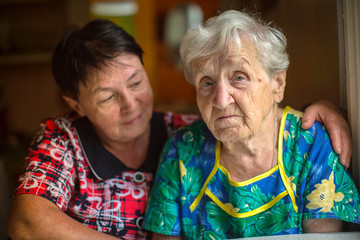 Sad elderly woman, in background hugging adult daughter.