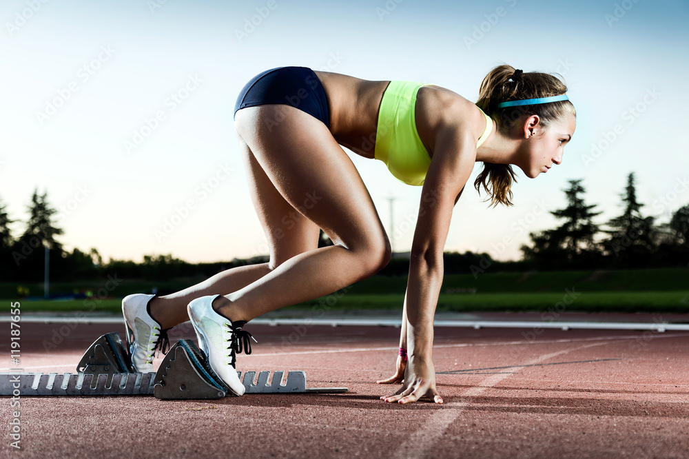 Young female athlete launching off the start line in a race. - obrazy, fototapety, plakaty 
