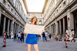 © rh2010 - Young female traveler in hat and blue dress standing with paper map near famous Uffizi museum in Florence. Vacation in Italy