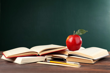 Wall Mural - School books with stationery and apple on blackboard background