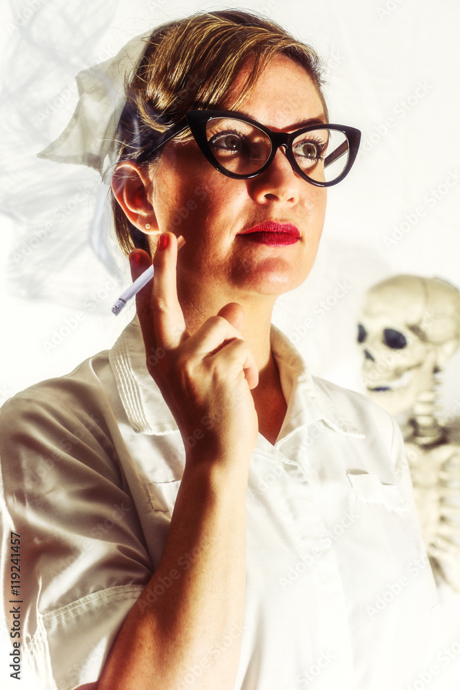 Vintage Nurse Smoking a Cigarette with Skeleton. Classic female nurse in  authentic vintage uniform smoking a cigarette with a skeleton behind her.  Edited in a vintage film style. Stock Photo