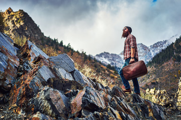 rugged traveler climbing rocky mountain carrying suitcase