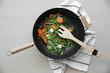 Vegetables and wooden spatula in pan  on wooden table, top view
