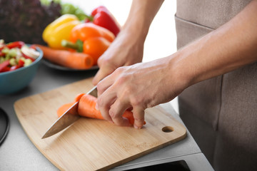 Sticker - Male hands cutting carrot on wooden board closeup