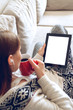 © perfectlab - Woman in home cozy clothes sitting on a sofa using tablet with headphones, holding a red cup of coffee hands. Online education concept. e-learning. back view