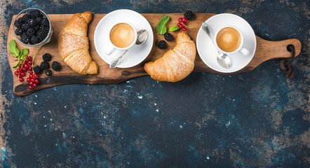 Wall Mural - Breakfast set. Freshly baked croissants with garden berries and coffee cups served on rustic wooden board over dark grunge plywood backdrop, top view, copy space