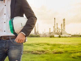 refinery engineer with white safety helmet see drawing standing in front of oil refinery building structure in heavy petrochemical refinery industry.