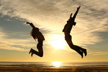 Couple Or Friends Jumping On The Beach At Sunset