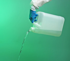 Hand in glove pouring water from jerrycan on green background