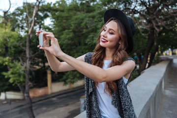 Wall Mural - Young beautiful brunette girl making selfie with her phone outdoors