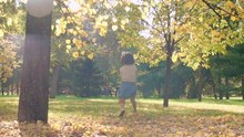 Slow Motion Of Smiling Little Girl Jumping And Throwing Fallen Leaves Around Herself On Bright Autumn Day In Park