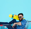 © kegfire - Side view of cheerful young man sitting in shopping cart