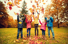 Happy Children Playing With Autumn Leaves In Park