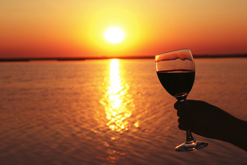 Wall Mural - Man hand with wine glass on sunset background