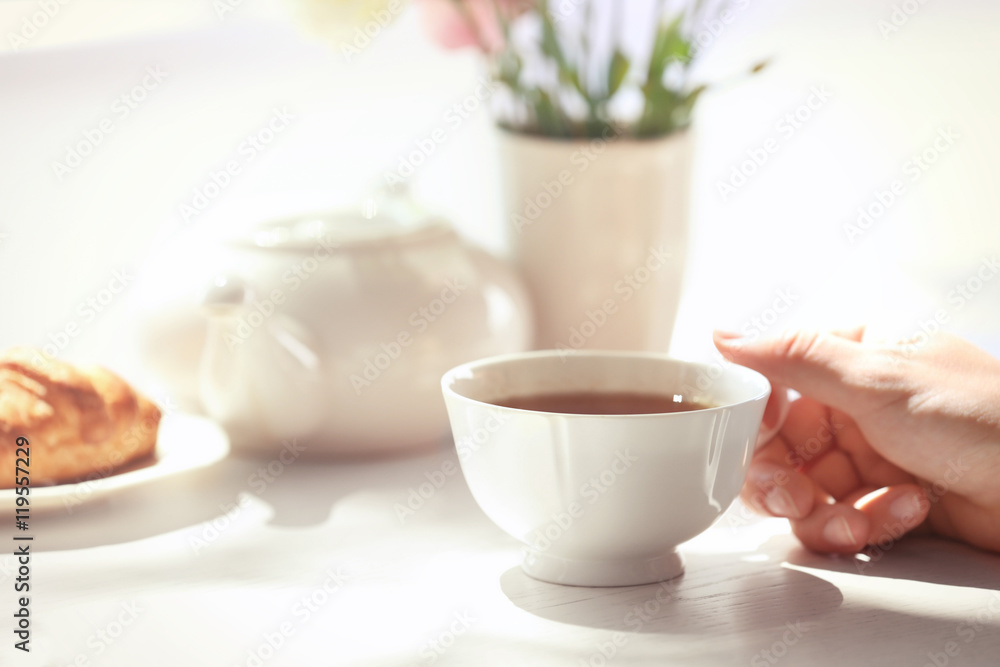 Female hand holding cup of tea on table