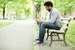 © Cavan Images - Side view of happy man using smart phone while sitting on park bench by footpath