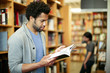 © Cavan Images - Man reading book in library with woman standing in background