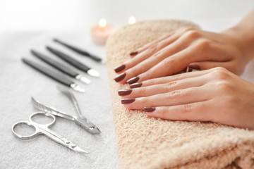 Canvas Print - Female hands with brown manicure on towel and instruments, closeup