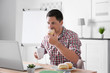 © Africa Studio - Handsome man eating in front of laptop