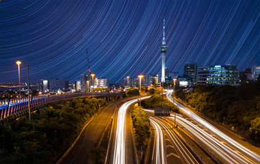 city skyline with traffic on highway and star trails on sky, auckland