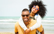© akhenatonimages - Young afro american couple playing piggyback ride on beach - Cheerful african friends having fun at day with blue ocean background - Concept of lovers happy moments on summer holiday - Vintage filter