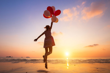 imagination, happy girl jumping with multicolored balloons at sunset on the beach, fly, follow your 